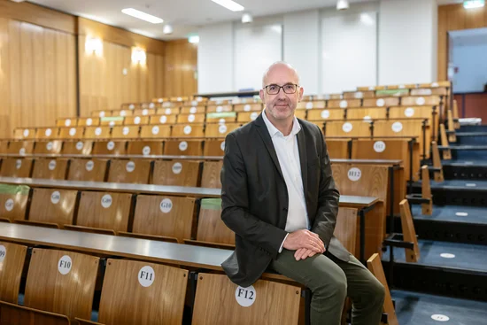 Ein Mann sitzt in einem leeren Hörsaal auf einem der Tische.